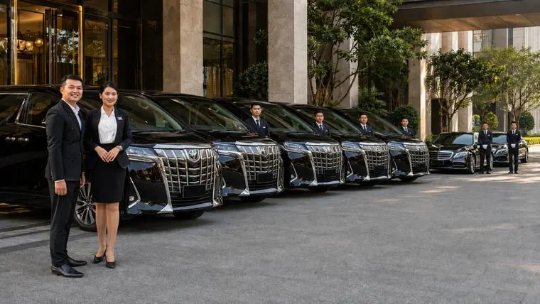 A fleet of black limousines with chauffeurs waiting at a hotel entrance